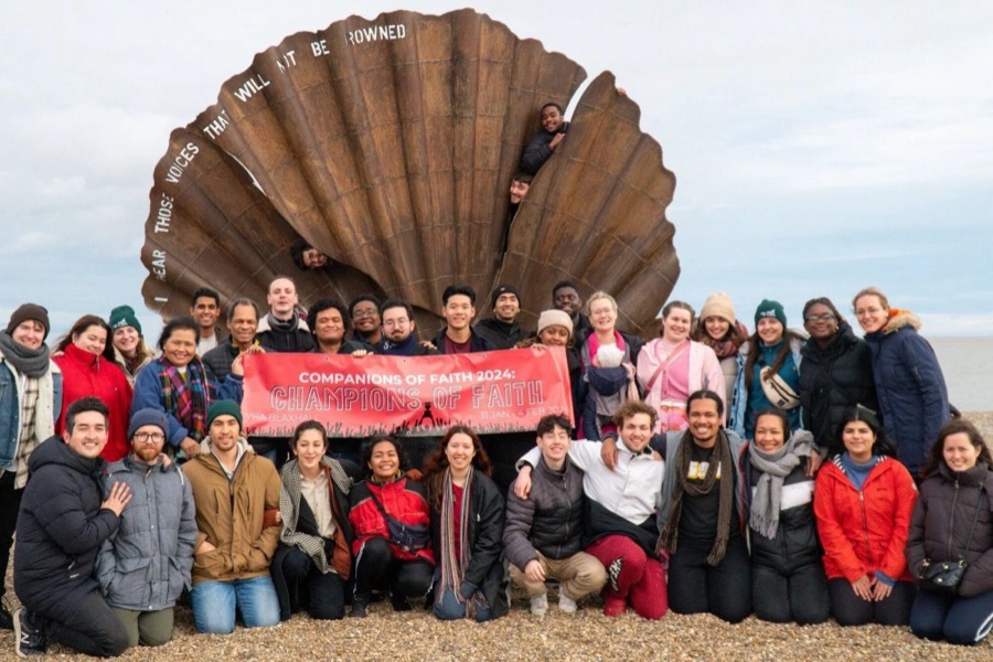 A gathering on a shingle beach beneath a shell sculpture