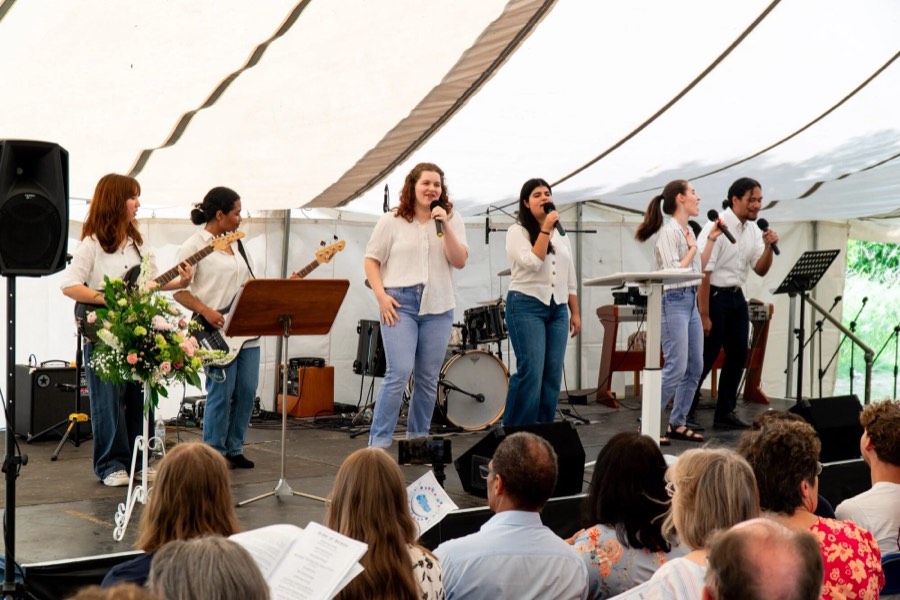 A band leading a congregation under a marquee